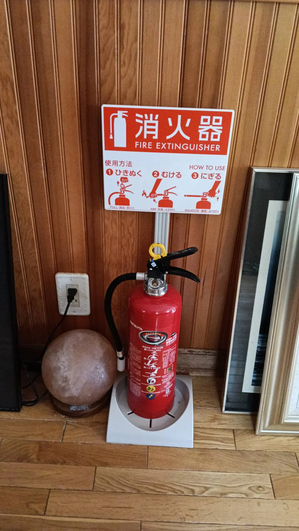 1階の板張りの壁ぎわに置かれた消火器と、使い方を示す案内板